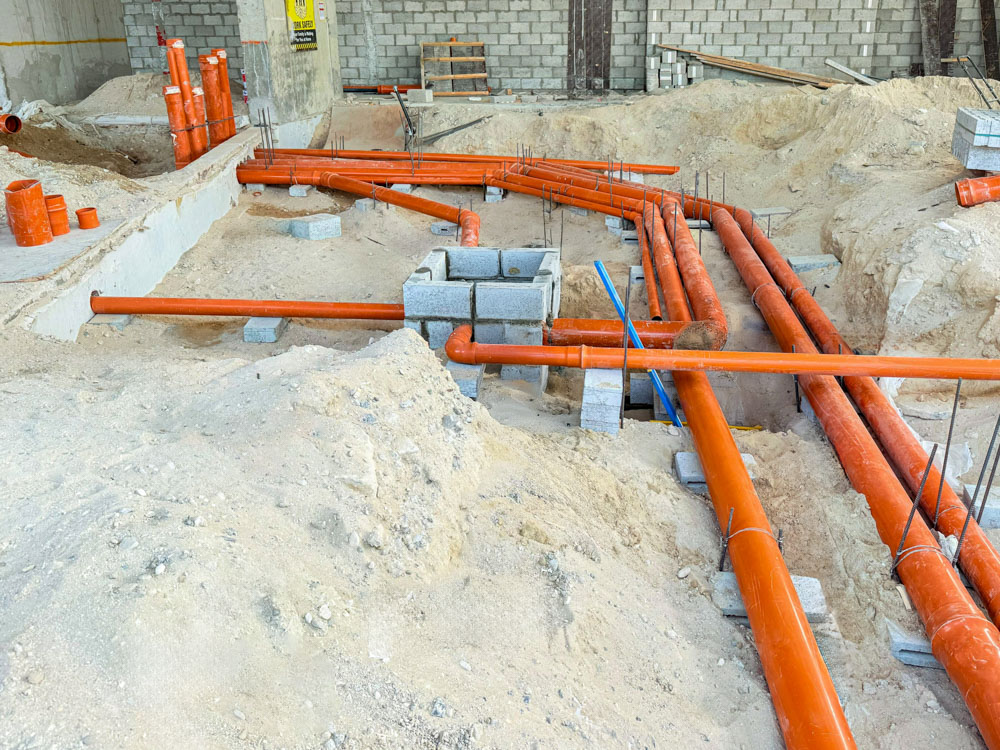 Beach Walk Iii By Imtiaz Construction site showing orange pipes, concrete blocks, and sand, indicating infrastructure work in progress.